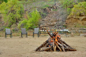 Bon fire set on a beach on the shores of Lake Kariba with table and chairs for drinks and relaxation are lined up close to the base of a hill